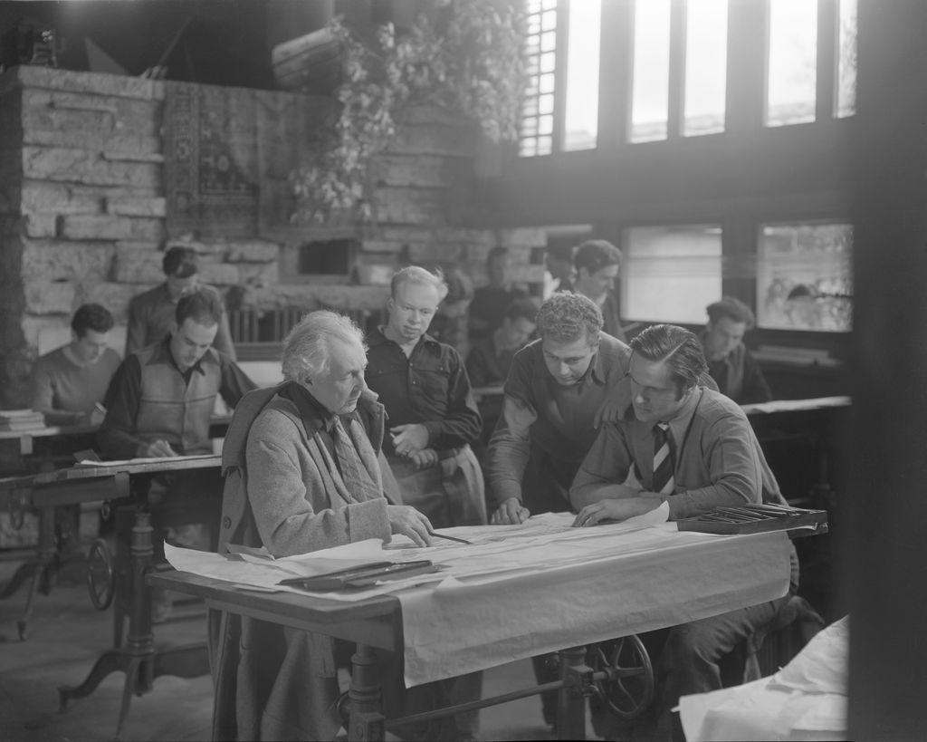 The architect Frank Lloyd Wright at a drafting table with several onlookers while at Taliesin East